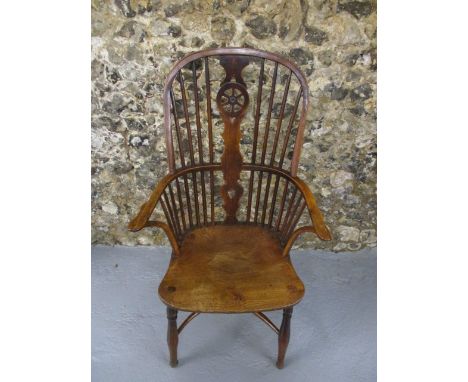 A late 18th century Windsor chair having a hoop, spindle and wheel splat, level arms, the solid seat raised on elliptical, tu