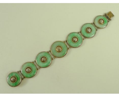 A Chinese jade bracelet, circa 1920s, formed as seven jade discs set within gilded white metal mounts, each disc with Chinese