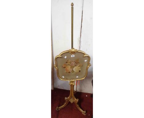 A giltwood and brass pole screen with floral tapestry panel under glass within a Rococo style border, set on tripod scroll ba
