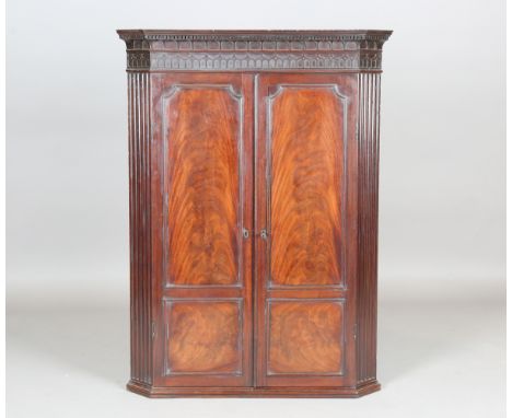 A George III Chippendale period figured mahogany hanging corner cabinet, the blind fretwork frieze above a pair of doors encl