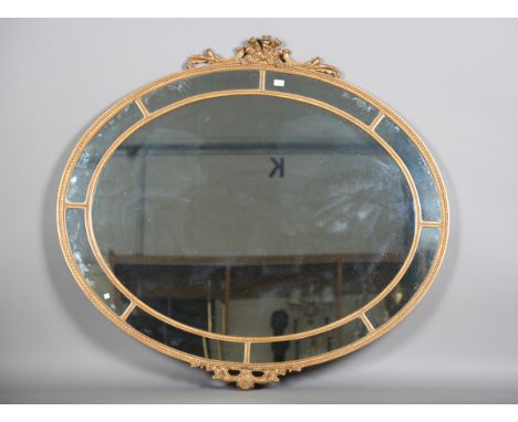A large late 20th century Neoclassical style gilt composition oval wall mirror, the sectional frame with a tied ribbon crest,