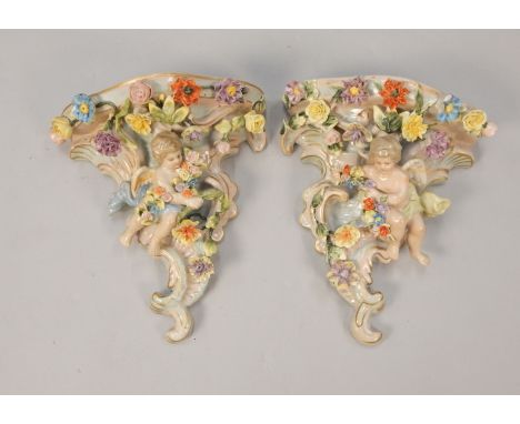 A pair of Sitzendorf type porcelain wall pockets, each decorated with putti and with flower encrusted borders, 22cm high