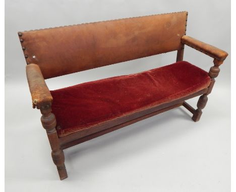 An early 20thC oak settle or bench, with a brown leatherette padded back, arm rests and loose cushion on turned legs