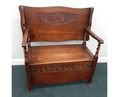 An oak monks bench, the rectangular top with a shaped edge, on spirally turned supports with hinged seat, 107cm wide.