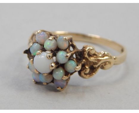 A 9ct gold dress ring, the floral cluster set with opal stones, with scroll designed shoulders, 1.7g all in.