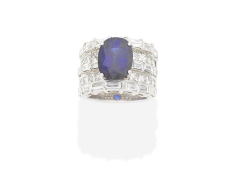 SAPPHIRE AND DIAMOND RINGThe oval-cut sapphire, issuing from tiered rows of baguette and princess-cut diamonds, sapphire appr