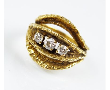 An 18ct gold three stone diamond ring, the three graduated brilliant cut diamonds claw set in yellow gold to textured split m