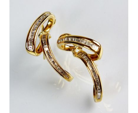 A pair of stylised diamond set earrings, each designed as two tapering baguette cut diamond set scrolls, channel set in yello