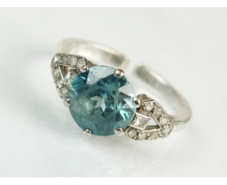 An Art Deco blue zircon and diamond ring, designed as a central round mixed cut faceted zircon, claw set in white metal to di