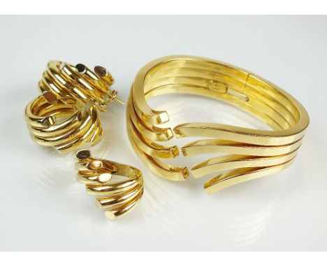 A suite of stylised wave design jewellery, comprising; a hinged bangle, a pair of hoop earrings and a ring, each stamped '750
