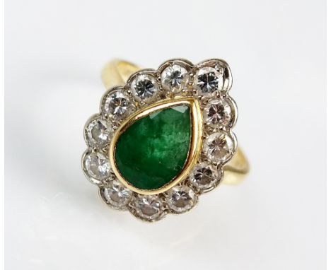 An emerald and diamond cluster ring, designed as a central pear cut emerald collet set in yellow metal within a border of twe