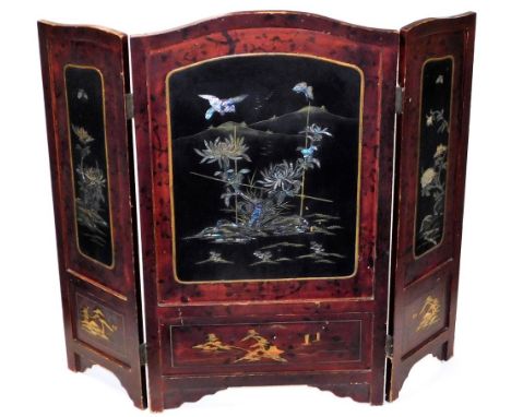 An early 20thC Japanese red and black lacquer three fold fire screen, with shaped top and three panels of flowering shrub and