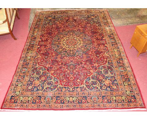 * A Persian woollen Tabriz style carpet, the red ground having central medallion issuing scroll flowers and foliage within tr