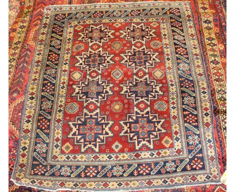 * A Turkish woollen rug, the red ground decorated with three rows of geometric medallions within multiple trailing borders, 1