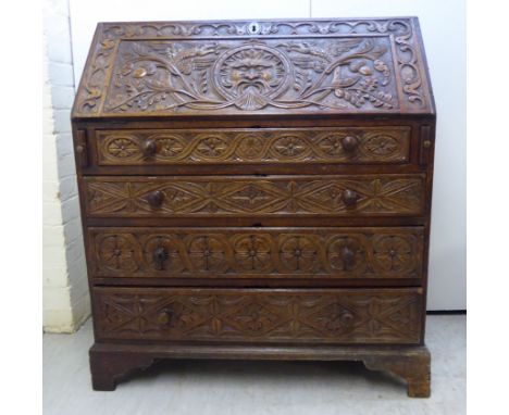 An early 19thC oak bureau, the profusely carved fall-flap enclosing a fitted interior, over four long graduated drawers, rais