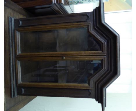 An early 20thC stained oak display cabinet, the breakfront top with a thumb moulded edge, over four glazed panels, enclosing 