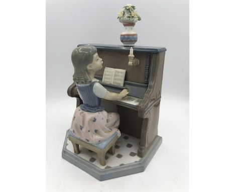 A Lladro figure of a young girl playing piano.