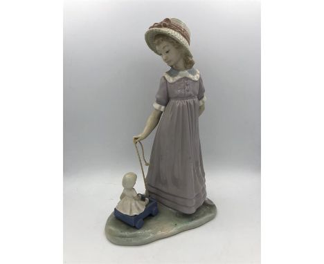 A Lladro figure of a girl playing with her doll in a cart.
