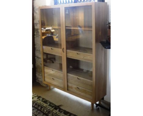 An Ercol display cabinet with two glazed doors enclosing adjustable shelving and six drawers, designed by Terence Conran, cir