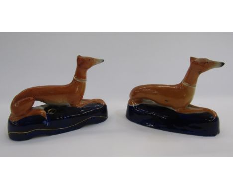 Pair of Staffordshire pottery greyhound pen rests, each ochre coloured hound seated on a dark blue mound base, pierced with g