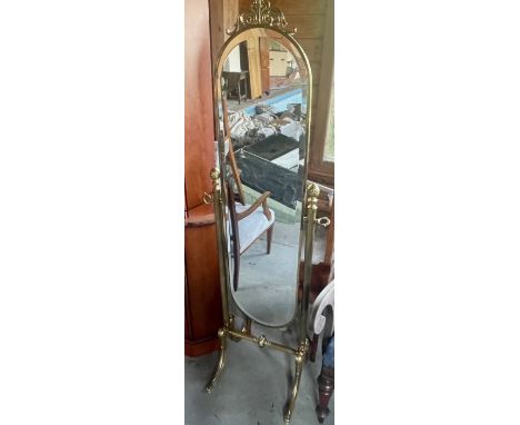 A Victorian revival brass standing mirror, scrolling crest on an arch shaped looking glass, held by reeded supports mounted w