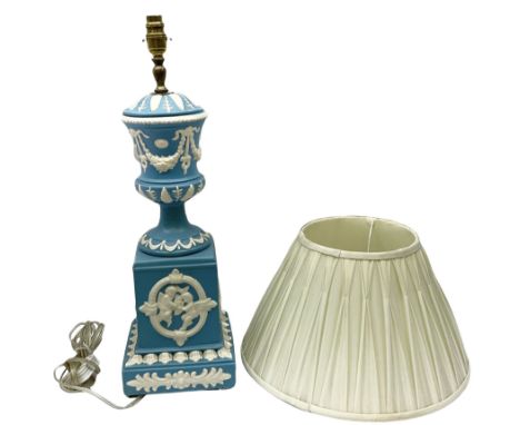 Ceramic urn shaped table lamp on a square pedestal base, decorated with relief studies of cherubs and foliage, on a blue grou