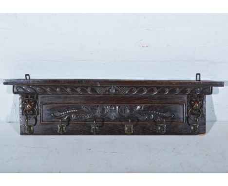 Carved oak cloak rail with a shelf over, decorated with lion masks, width 102cm, depth 14.5cm.