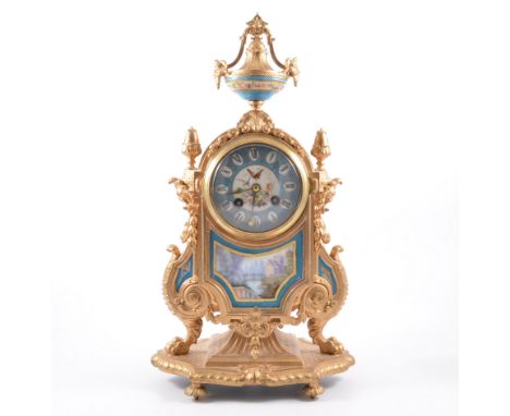 A French gilt metal mantel clock, inset with Servres style porcelain panels surmounted by a similar urn, circular dial painte