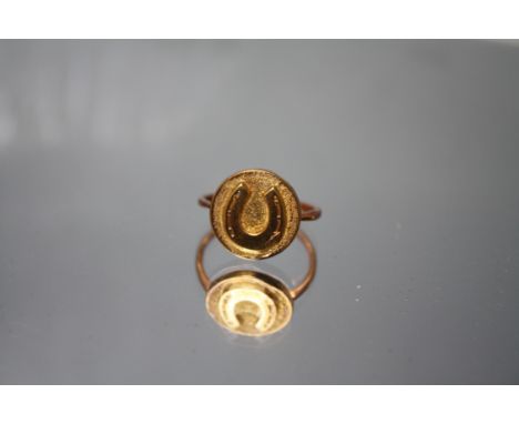 A VINTAGE YELLOW METAL EQUESTRIAN THEME RING, the yellow metal circular design with horseshoe emblem in relief, set on a rose