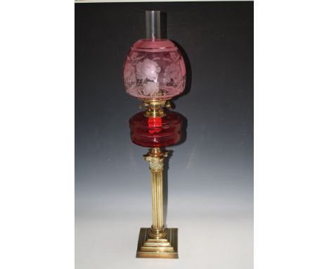 A VICTORIAN BRASS AND CRANBERRY GLASS PEDESTAL OIL LAMP, having cranberry tinted floral design acid etched shade and thumb-cu