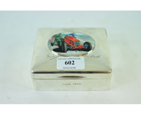 A silver cigarette box, later applied a plaque decorated a racing car, 12 cm wide