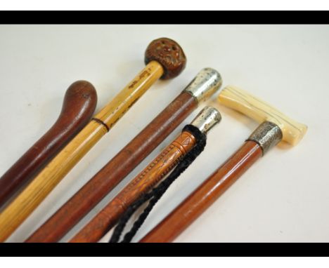 A holly walking stick, carved foliage, with a silver coloured metal cap, 86 cm long, and four other walking sticks (5)