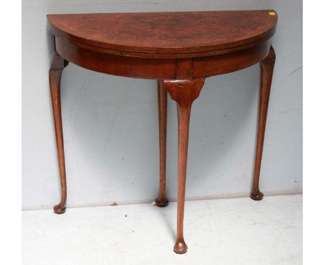 A 1930's demi-lune walnut folding card table with hinged burr walnut top enclosing green playing surface, raised on cabriole 