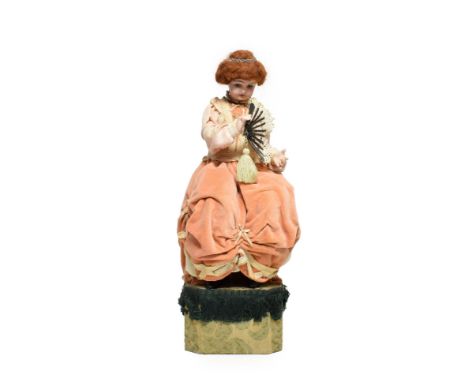 A Seated Doll Musical Automaton, with fan, beadwork headdress, necklace, dress with peach hued ruffed fabric with lace edging