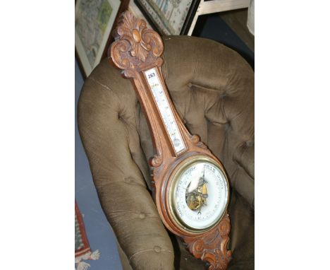 A LATE VICTORIAN CARVED OAK ANEROID BANJO BAROMETER WITH THERMOMETER SIGNED FENN, WEMBLEY