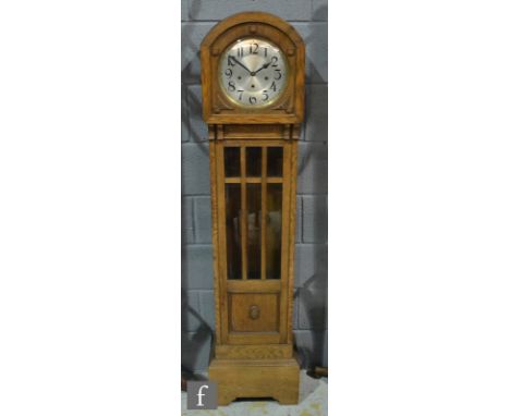 A 1930s oak longcase clock with eight day striking movement and circular silvered dial over a bar glazed door on plinth base,