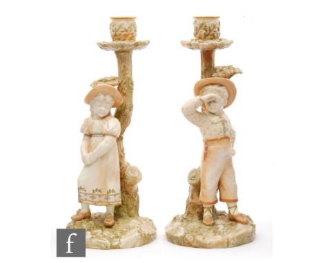 A pair of late 19th Century Royal Worcester candlesticks modelled by James Hadley, each with a child stood before a tree bran