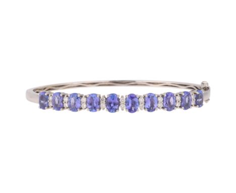 A 14ct white gold tanzanite and diamond hinged bangle, set with oval mixed-cut tanzanites separated by modern round brilliant