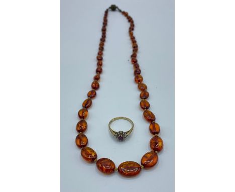 A 9ct gold ruby and diamond set flower ring. Size P. 0.80g and A graduated amber bead necklace. 56cm. Approx 5g. 