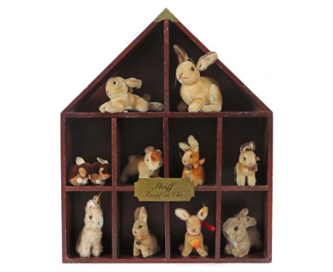 Diorama mit 9 Hasen und 2 WollminisSteiff, Holzschaukasten in Form eines Hauses mit 10 offenen Fächern, Frontschild: Steiff-K