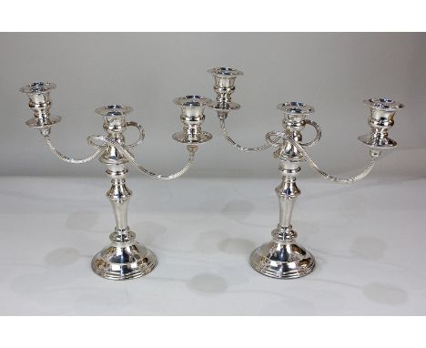 A pair of silver plated three-light candelabra with scroll branches, urn shape sconces with drip pans, on baluster stems and 