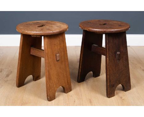 A pair of Art and Crafts style oak low stools, the circular top with carrying handle on two wide supports with bracket feet u