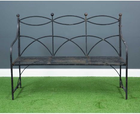 A three-seater black painted metal garden bench, with strap metal seat and arching cut out back topped with ball finials on b