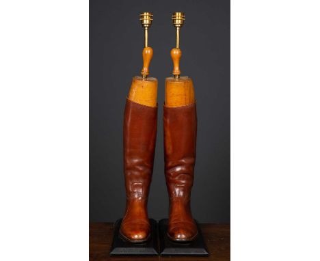 A pair of decorative table lamps constructed from brown leather riding boots, mounted on rectangular plinth bases, 78.5cm hig