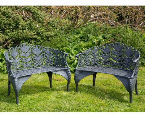 A pair of green painted cast iron garden benches with mask terminals to the arms, the backs with laurel fronds and the front 