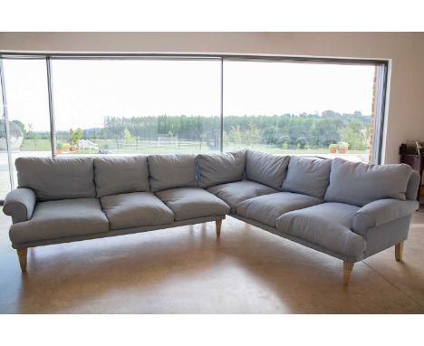 A light blue upholstered L shaped six seater sofa standing on turned tapering oak front legs, with scrolling arms, originally