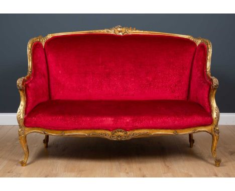 A 19th century French style gilt framed small sofa with carved ornament and overstuffed upholstery to the back, arms and shap