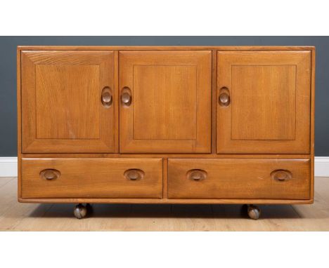 A 1970's Ercol light elm three-door sideboard, the pair of cupboard doors and single cupboard door (with fitted cutlery drawe