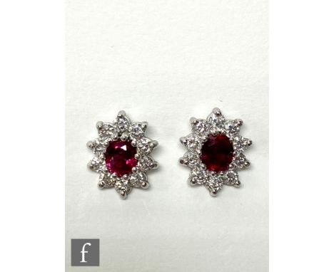 A pair of 18ct hallmarked white gold ruby and diamond cluster stud earrings, central oval rubies within a border of ten brill