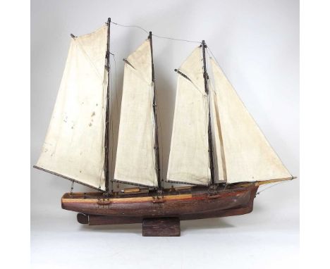 An early 20th century wooden model of a three masted schooner, with sails and rigging, on a wooden stand, 81cm long overall